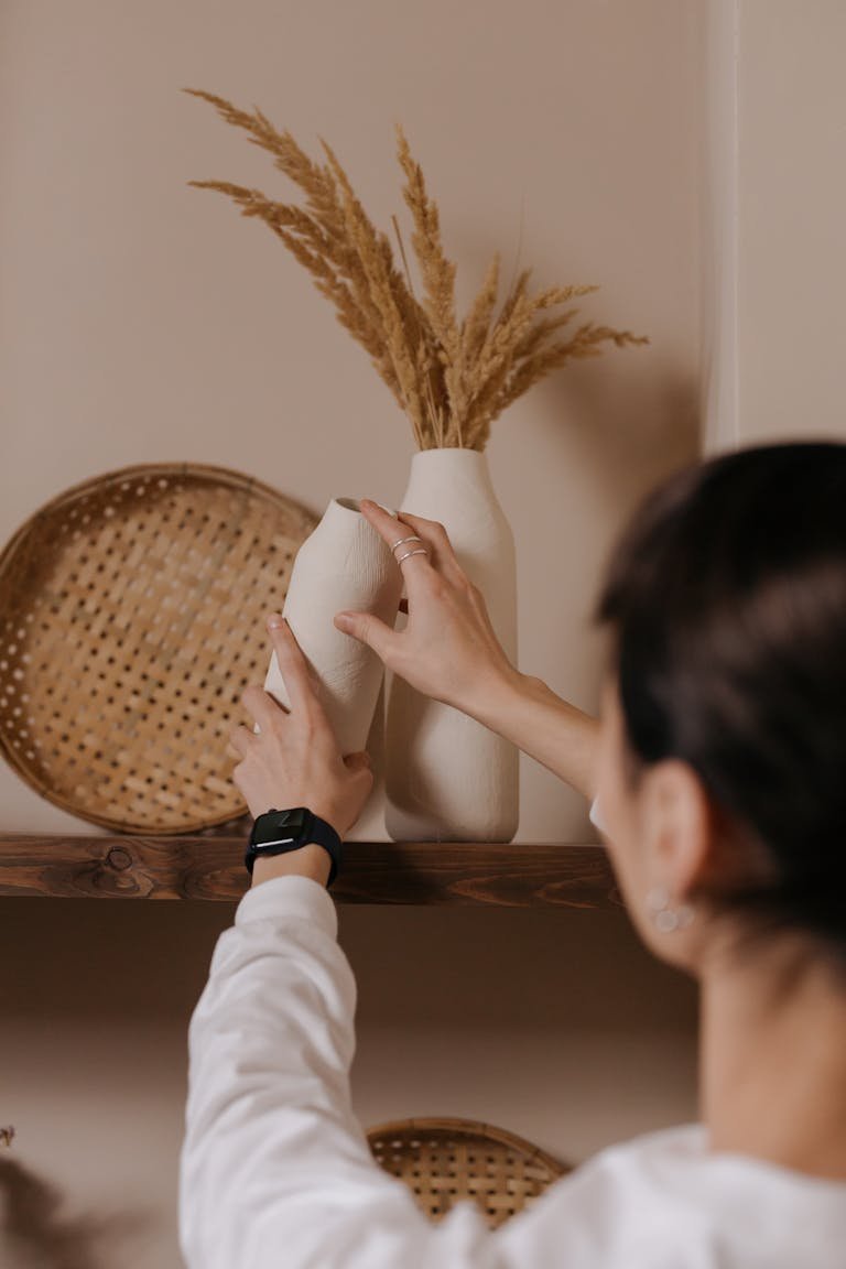A woman in a white sweater arranges vases on a shelf, showcasing modern home decor.